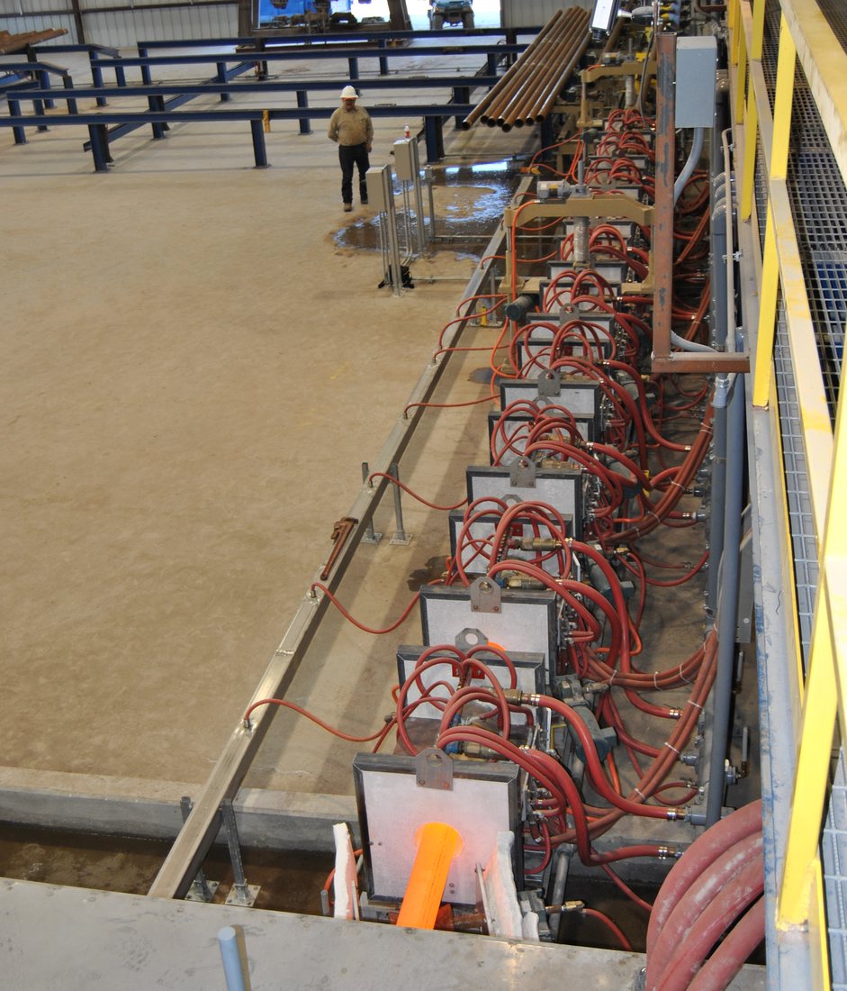 Induction heating line with water-cooled coil stations, hot pipe at temperature, and the runout and cooling bed beyond